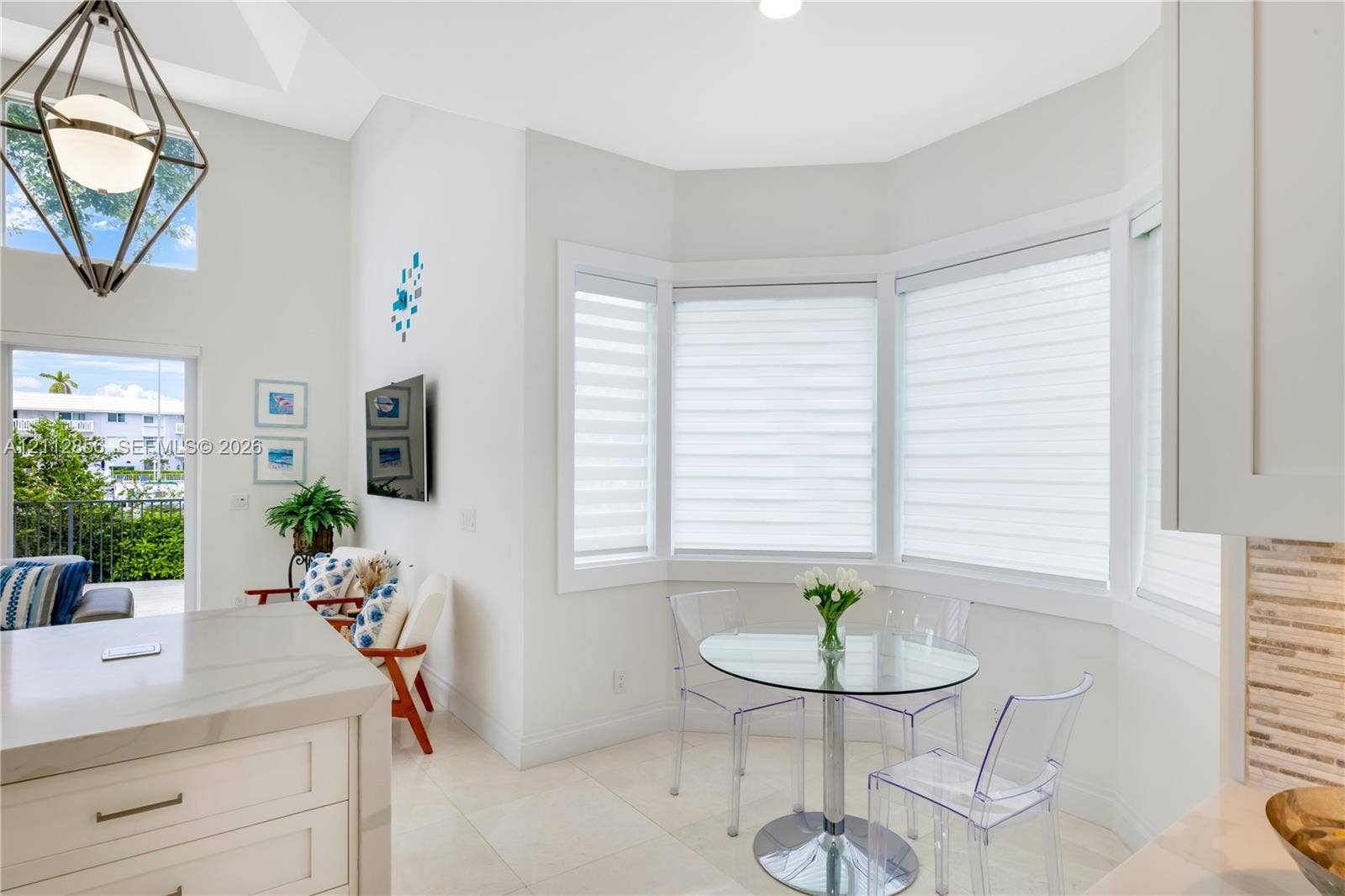 285 Las Brisas Court, Coral Gables, FL 33143 High-ceilinged room featuring a bay window, light-toned tile flooring, a geometric pendant light fixture, and a kitchen island with a stone-finish countertop
