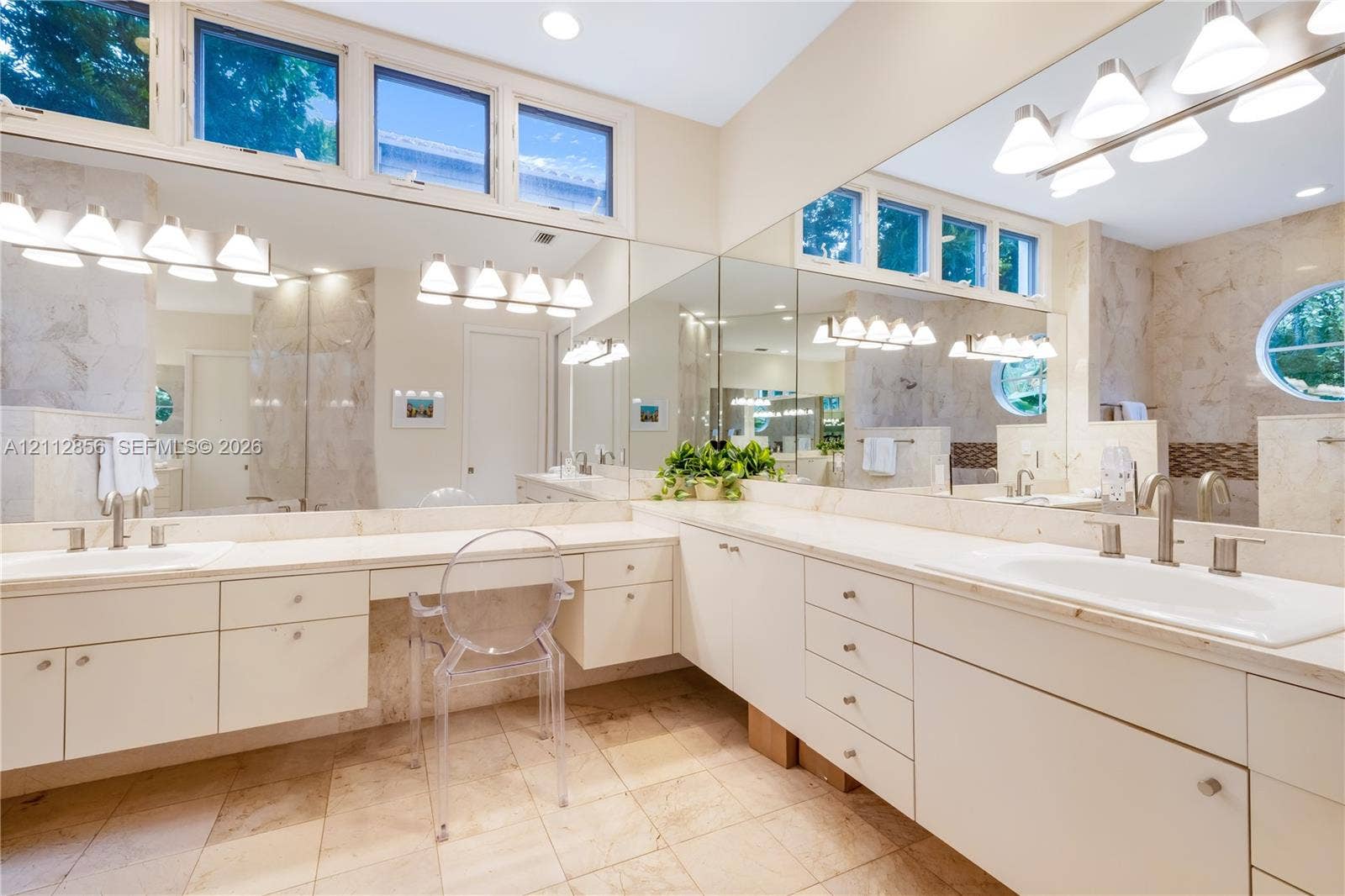 285 Las Brisas Court, Coral Gables, FL 33143 L-shaped vanity featuring a solid surface countertop, dual integrated sinks with brushed metal faucets, extensive built-in cabinetry, large-scale wall mirrors, and transom windows
