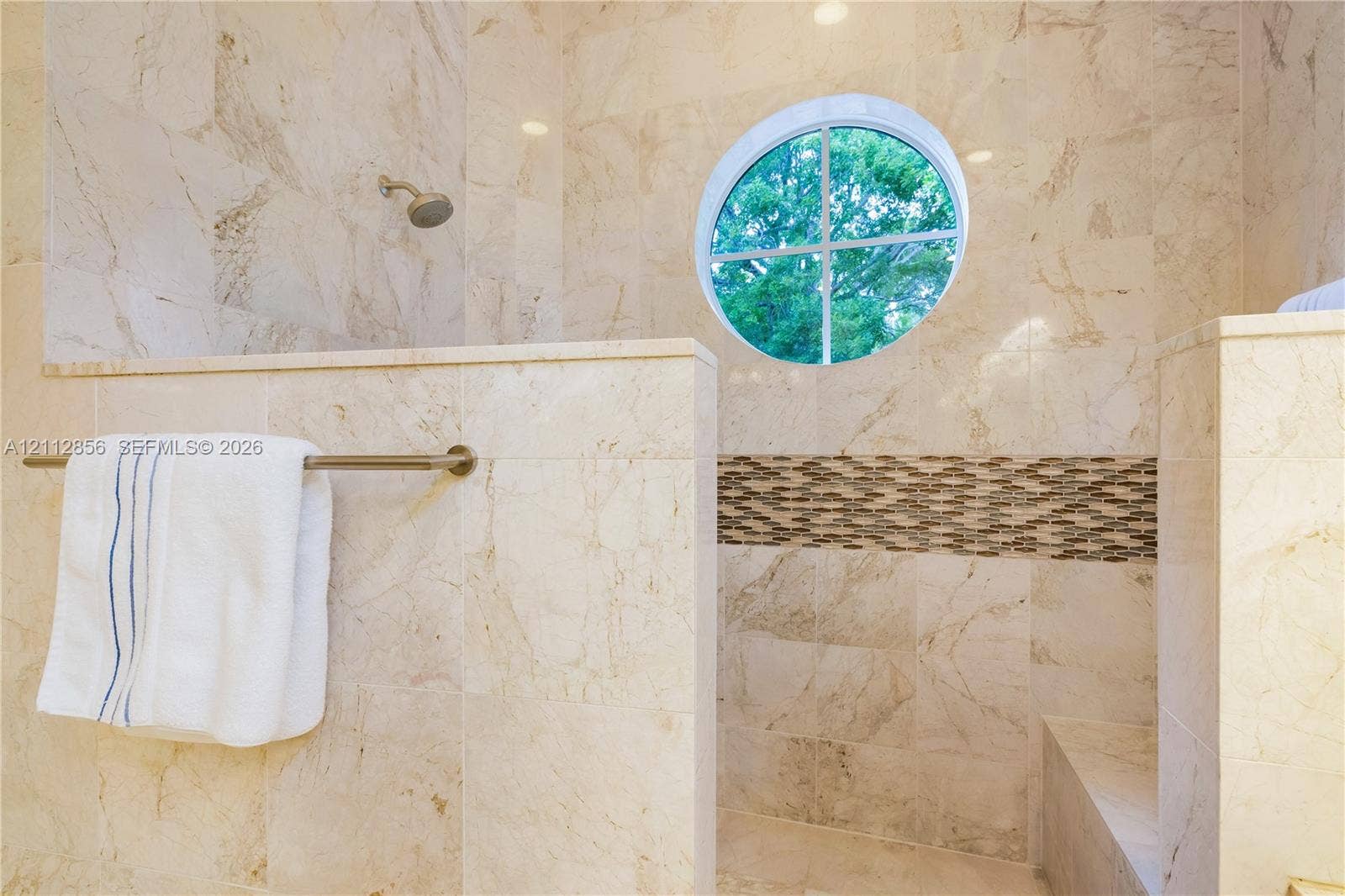 285 Las Brisas Court, Coral Gables, FL 33143 Walk-in shower featuring floor-to-ceiling stone tile, circular accent window, horizontal decorative stone inlay, built-in tiled bench, and wall-mounted shower head