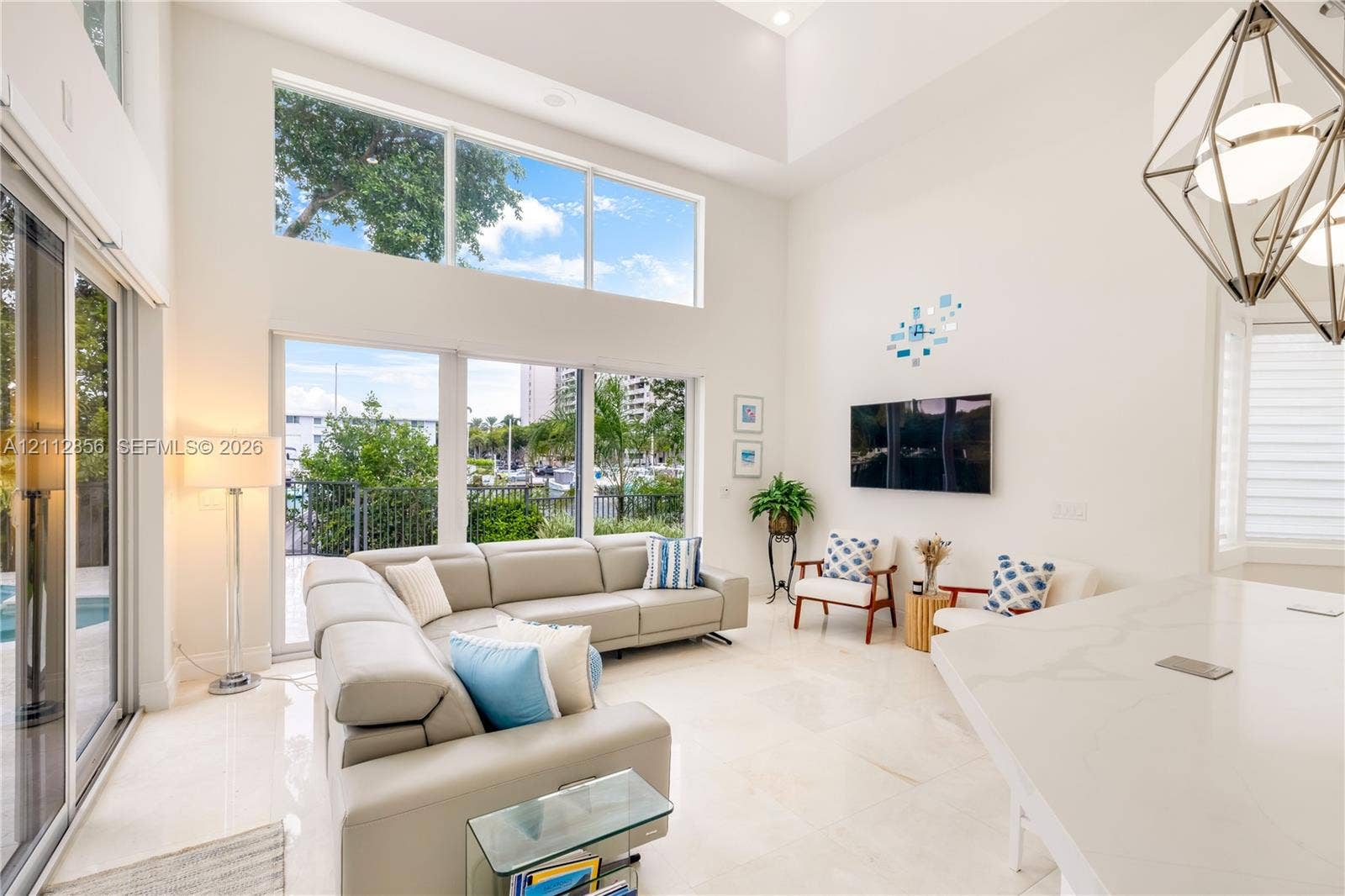 285 Las Brisas Court, Coral Gables, FL 33143 Double-height ceilings, extensive window wall, light-toned stone-finish flooring, and geometric pendant lighting