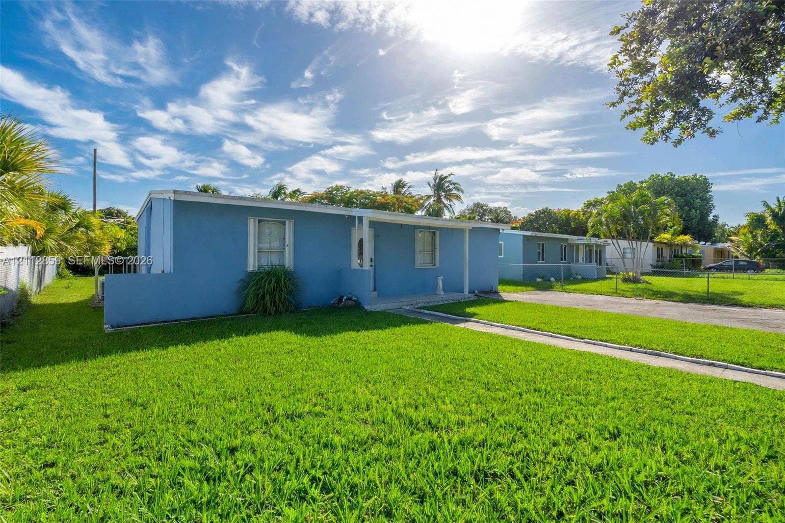 1207 Chateau Park Drive, Fort Lauderdale, FL 33311 Exterior view featuring a blue-toned facade, horizontal window placements, concrete walkway, and expansive green lawn with mature palm trees