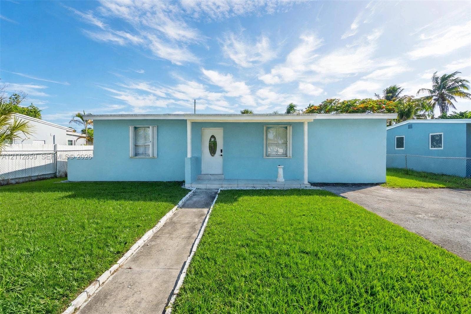 1207 Chateau Park Drive, Fort Lauderdale, FL 33311 Single-story exterior featuring a light blue stucco facade, covered front entryway, concrete walkway, and asphalt driveway