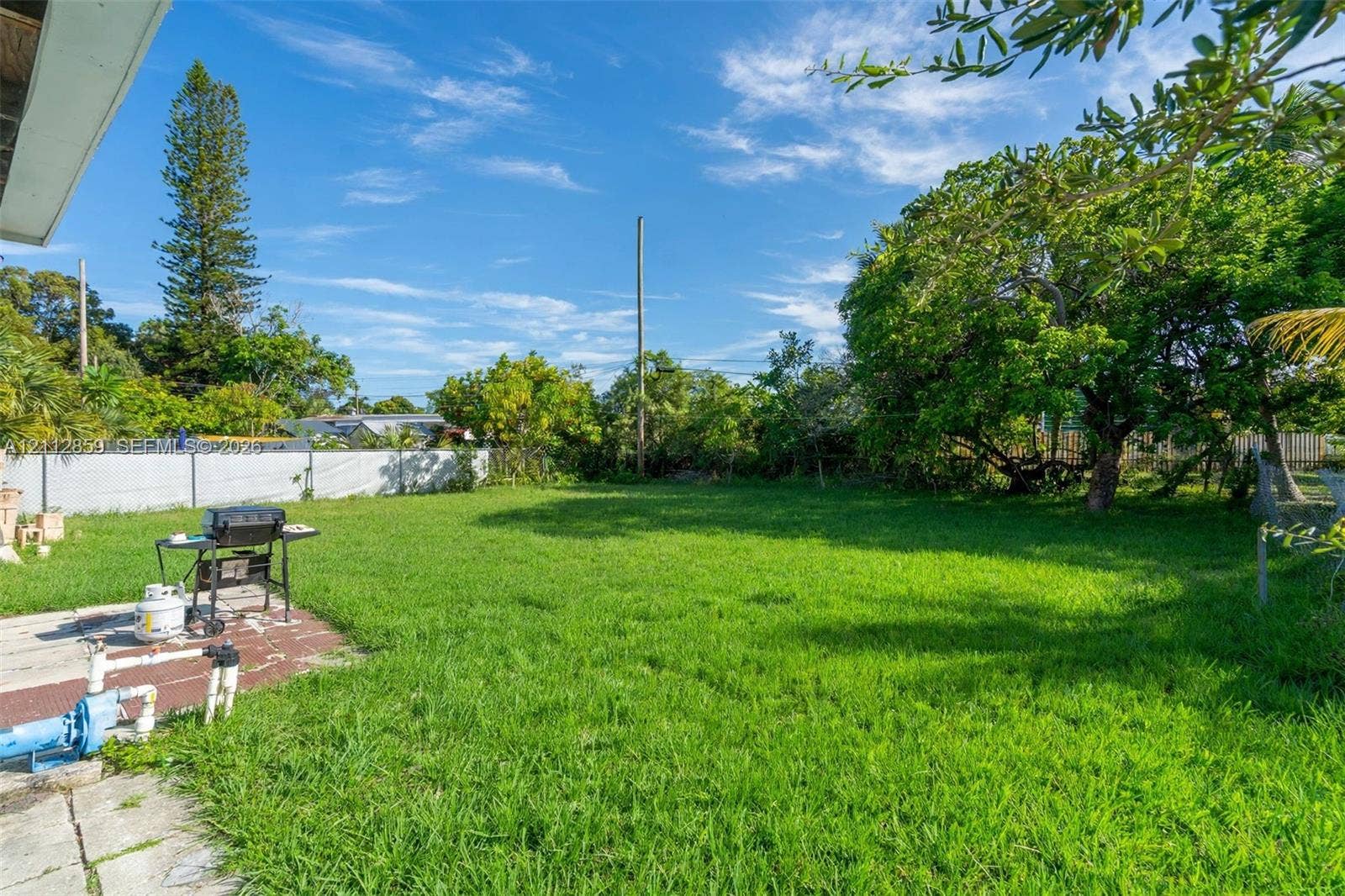 1207 Chateau Park Drive, Fort Lauderdale, FL 33311 Expansive backyard featuring a large grass lawn, mature trees, and perimeter chain-link fencing