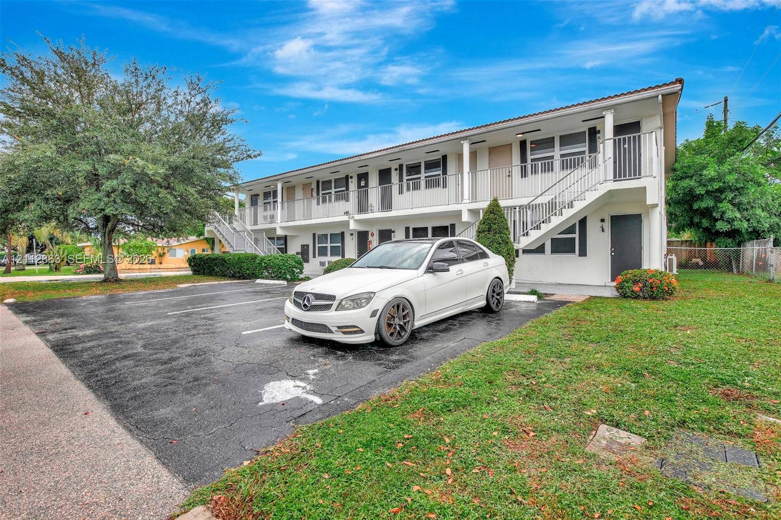 1520 NE 56th Street, #4, Fort Lauderdale, Fort Lauderdale, FL 33334 Two-story exterior featuring white stucco siding, metal staircases with railings, paved surface parking, and mature landscaping