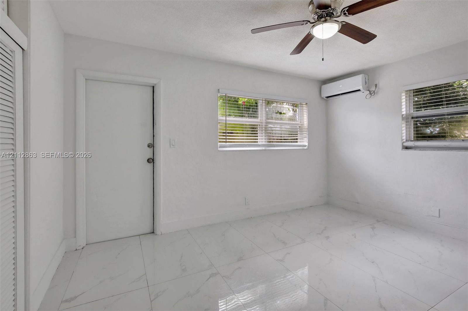 1520 NE 56th Street, #4, Fort Lauderdale, Fort Lauderdale, FL 33334 Room featuring large-format white tile flooring, wall-mounted ductless air conditioning unit, ceiling fan with integrated lighting, and louvered closet doors