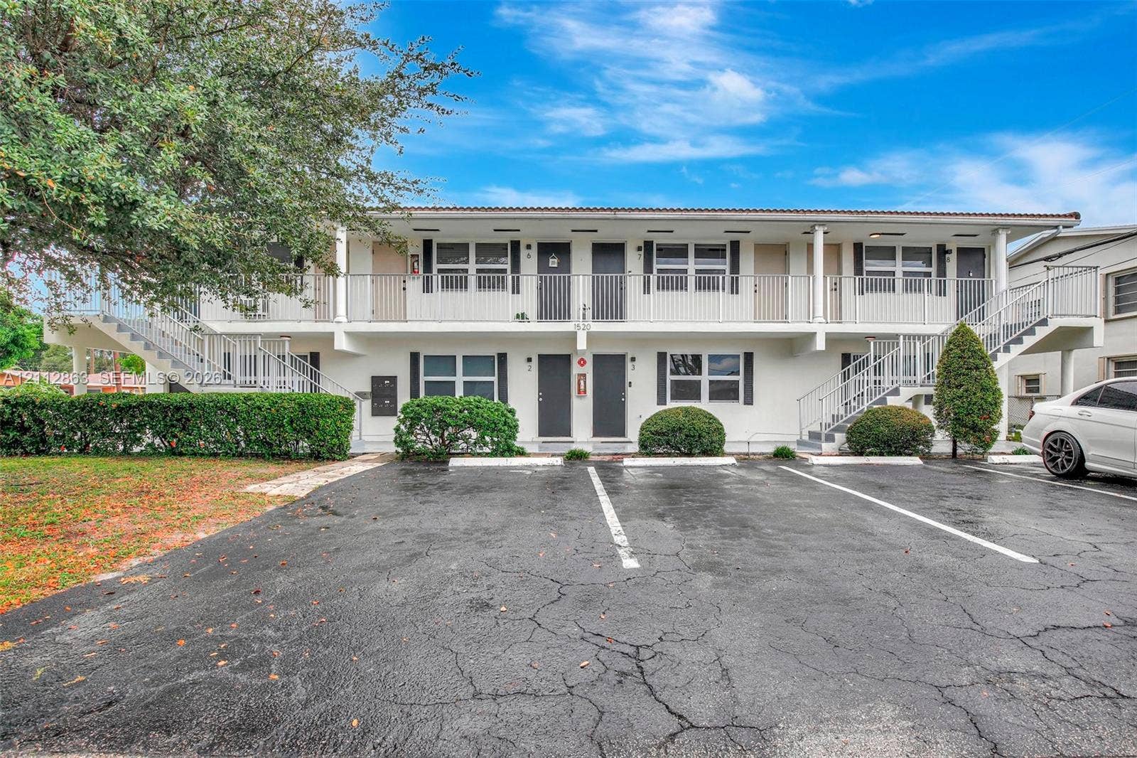 1520 NE 56th Street, #4, Fort Lauderdale, Fort Lauderdale, FL 33334 Two-story exterior featuring white stucco siding, dual-level railed balconies, paved surface parking, and manicured shrubbery