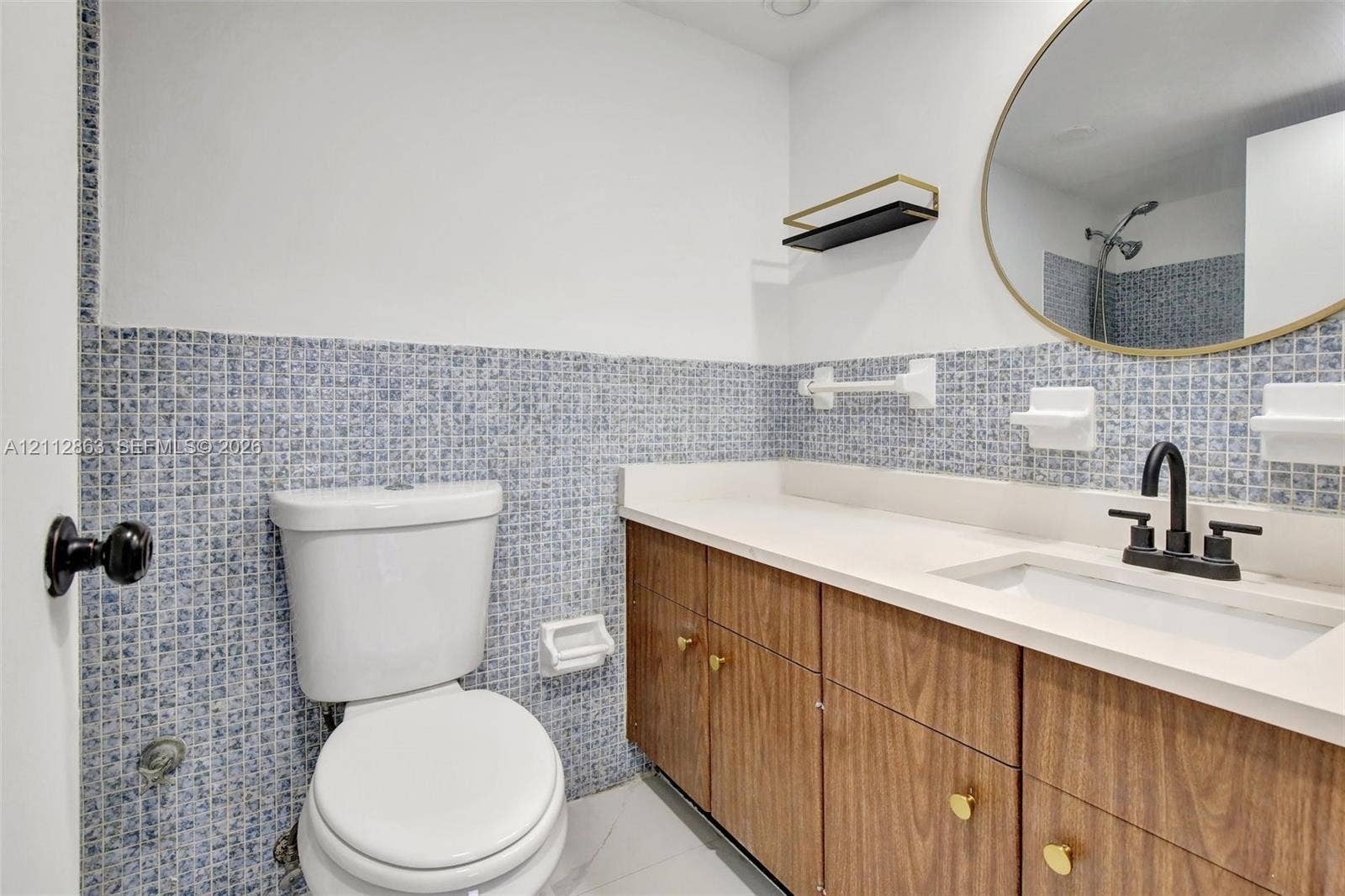 1520 NE 56th Street, #4, Fort Lauderdale, Fort Lauderdale, FL 33334 Vanity featuring wood-finish cabinetry, a solid surface countertop with an integrated basin, a matte black faucet, a gold-rimmed oval mirror, and blue mosaic tile wall accents
