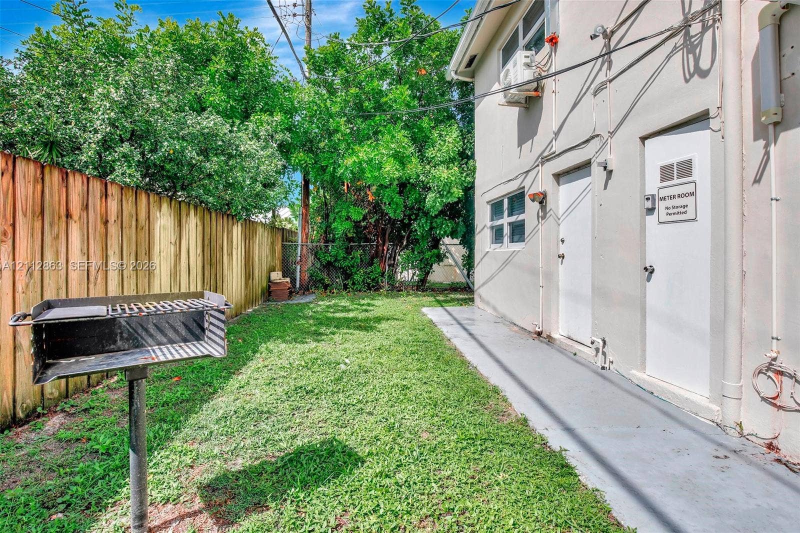 1520 NE 56th Street, #4, Fort Lauderdale, Fort Lauderdale, FL 33334 Exterior side yard featuring a wood-panel fence, a stationary metal grill, and a concrete walkway