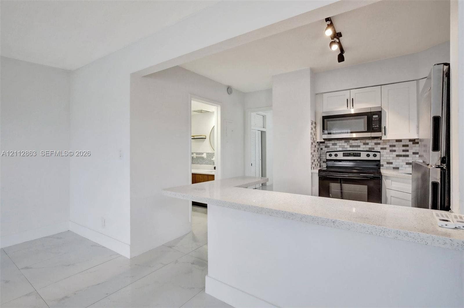 1520 NE 56th Street, #4, Fort Lauderdale, Fort Lauderdale, FL 33334 Kitchen featuring white shaker-style cabinetry, a quartz countertop breakfast bar, a stone-tiled backsplash, stainless steel appliances, and large-format porcelain floor tiling