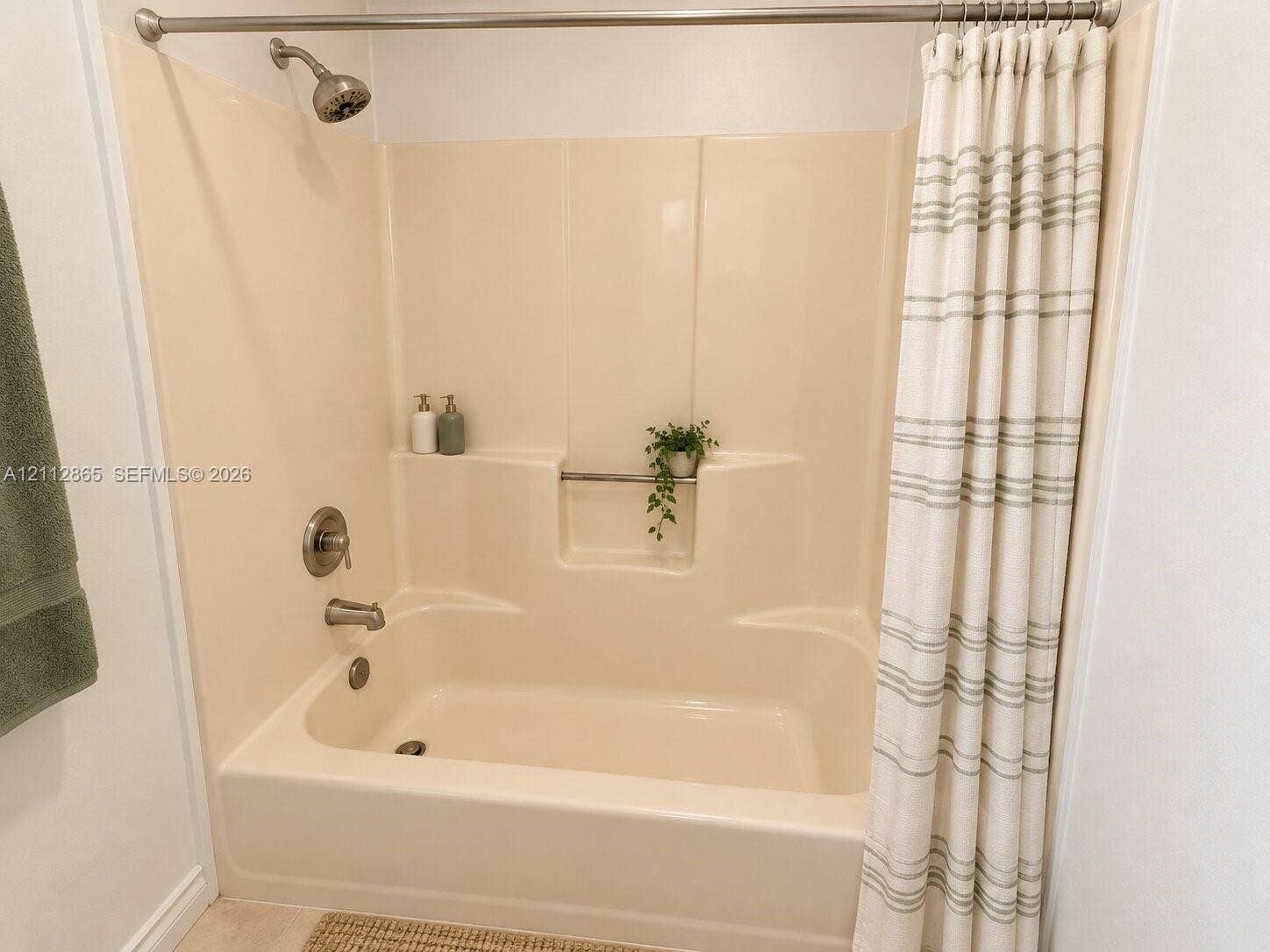 Bathtub and shower combination featuring a molded surround, integrated storage niche, and brushed nickel hardware