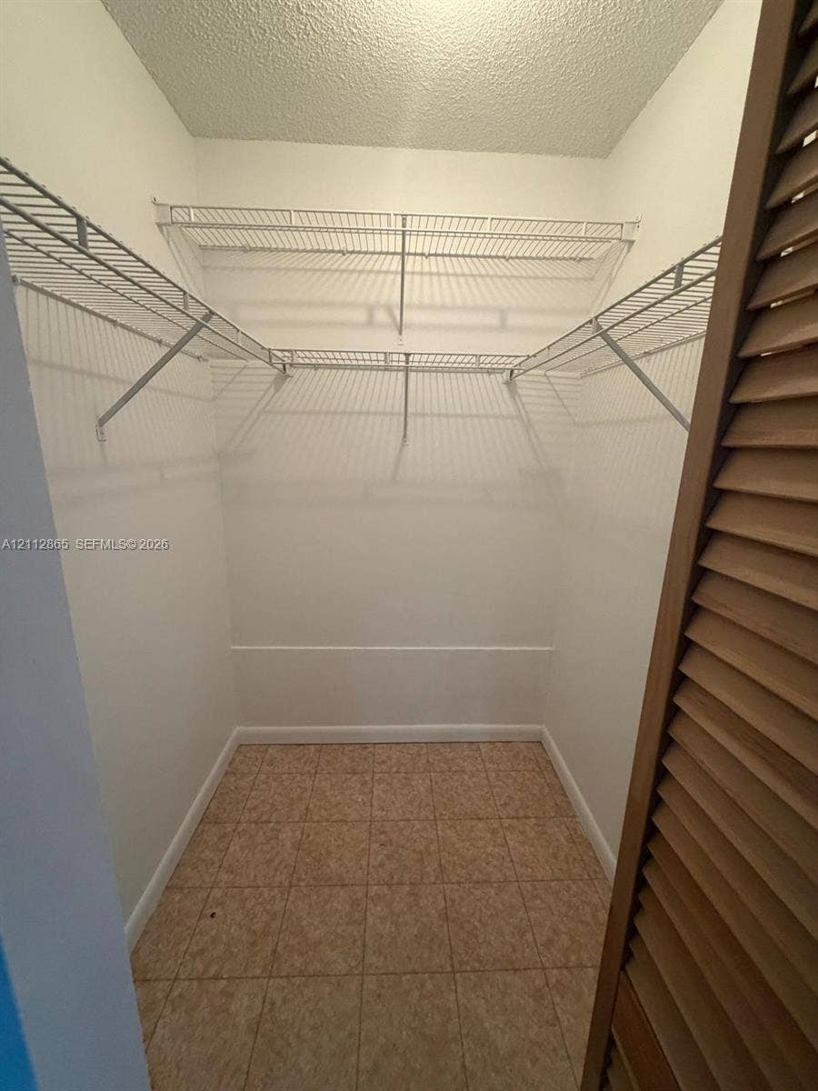 Walk-in closet featuring floor-to-ceiling white walls, ceramic tile flooring, and integrated white wire shelving