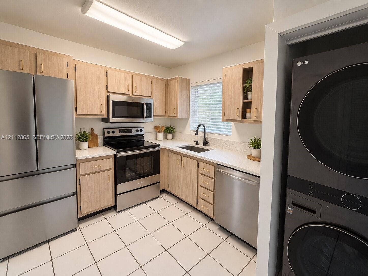 Kitchen featuring light-finish wood cabinetry, solid-surface countertops, stainless steel appliances, a deep basin sink with a matte black faucet, and ceramic tile flooring