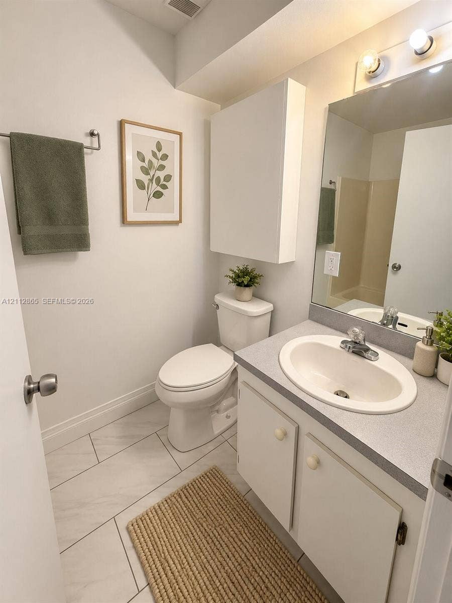 Bathroom featuring a vanity with a solid-surface countertop, an integrated oval sink, a wall-mounted storage cabinet, and large-format tile flooring