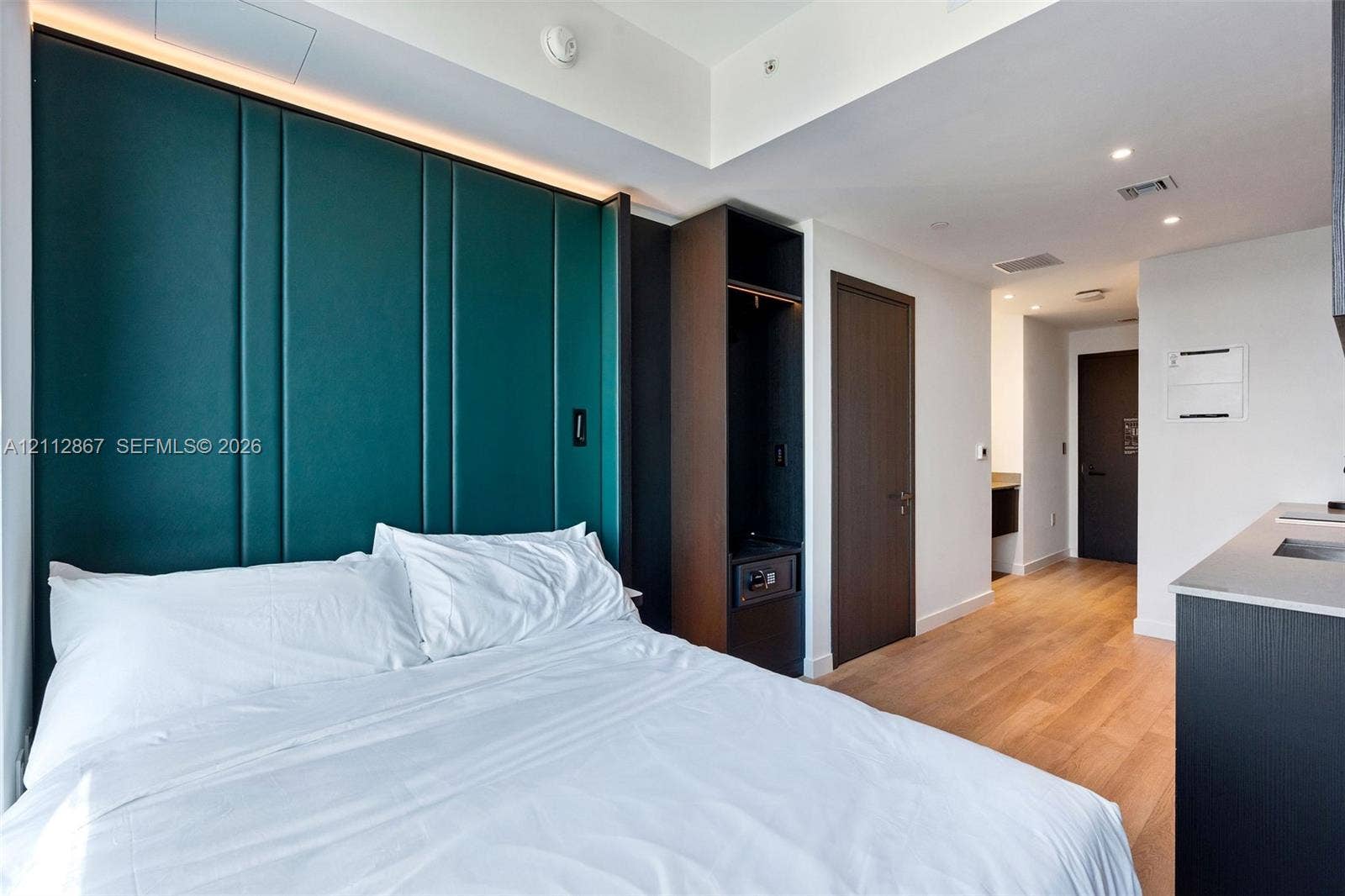 Deep teal paneled accent wall with integrated cove lighting, light wood-finish flooring, and dark wood-finish built-in cabinetry