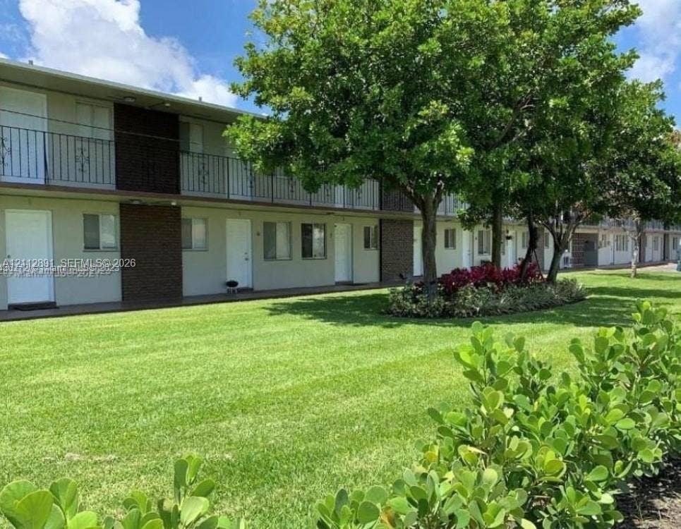 2150 Madison Street, #26, Hollywood, Hollywood, FL 33020 Two-story exterior featuring a metal balcony, manicured lawn, mature trees, and curated landscaping