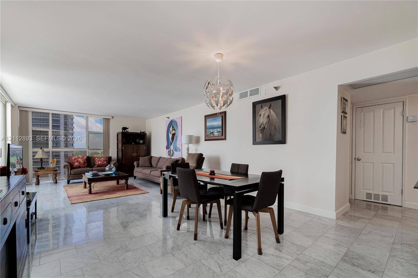 20515 E Country Club Drive, #1048, Aventura, FL 33180 Open-concept interior featuring light-toned stone flooring, floor-to-ceiling windows, and a spherical multi-light pendant fixture