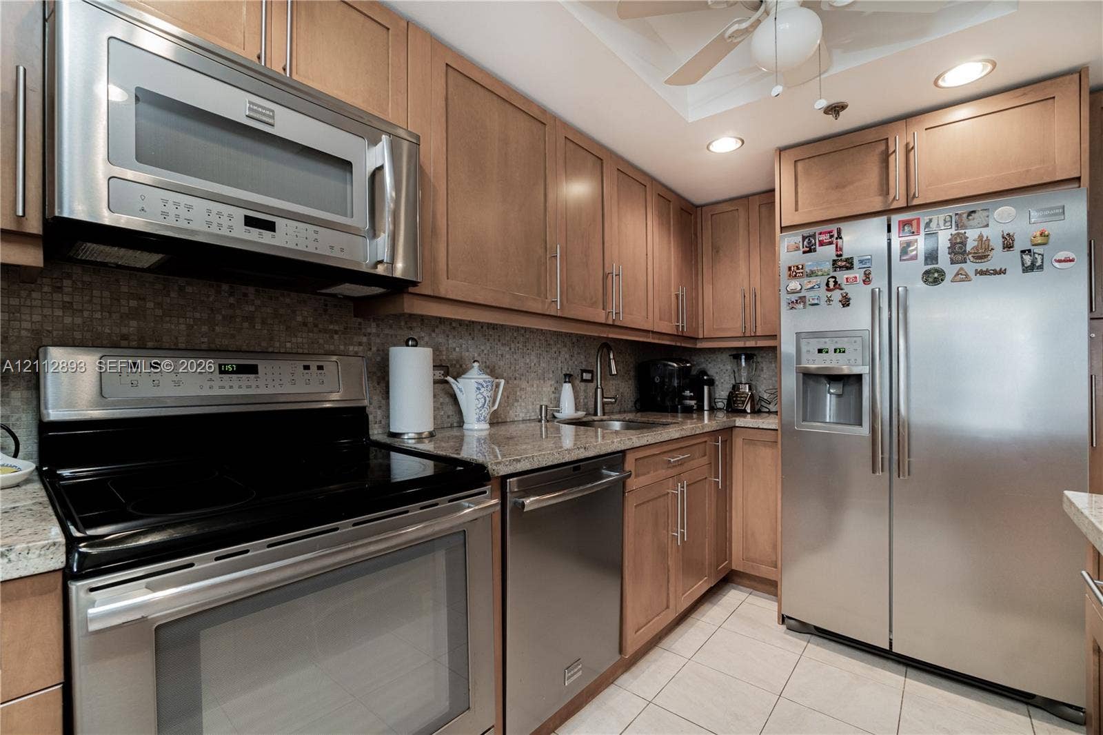 20515 E Country Club Drive, #1048, Aventura, FL 33180 Kitchen featuring wood cabinetry, stone countertops, a mosaic tile backsplash, stainless steel appliances, and tile flooring