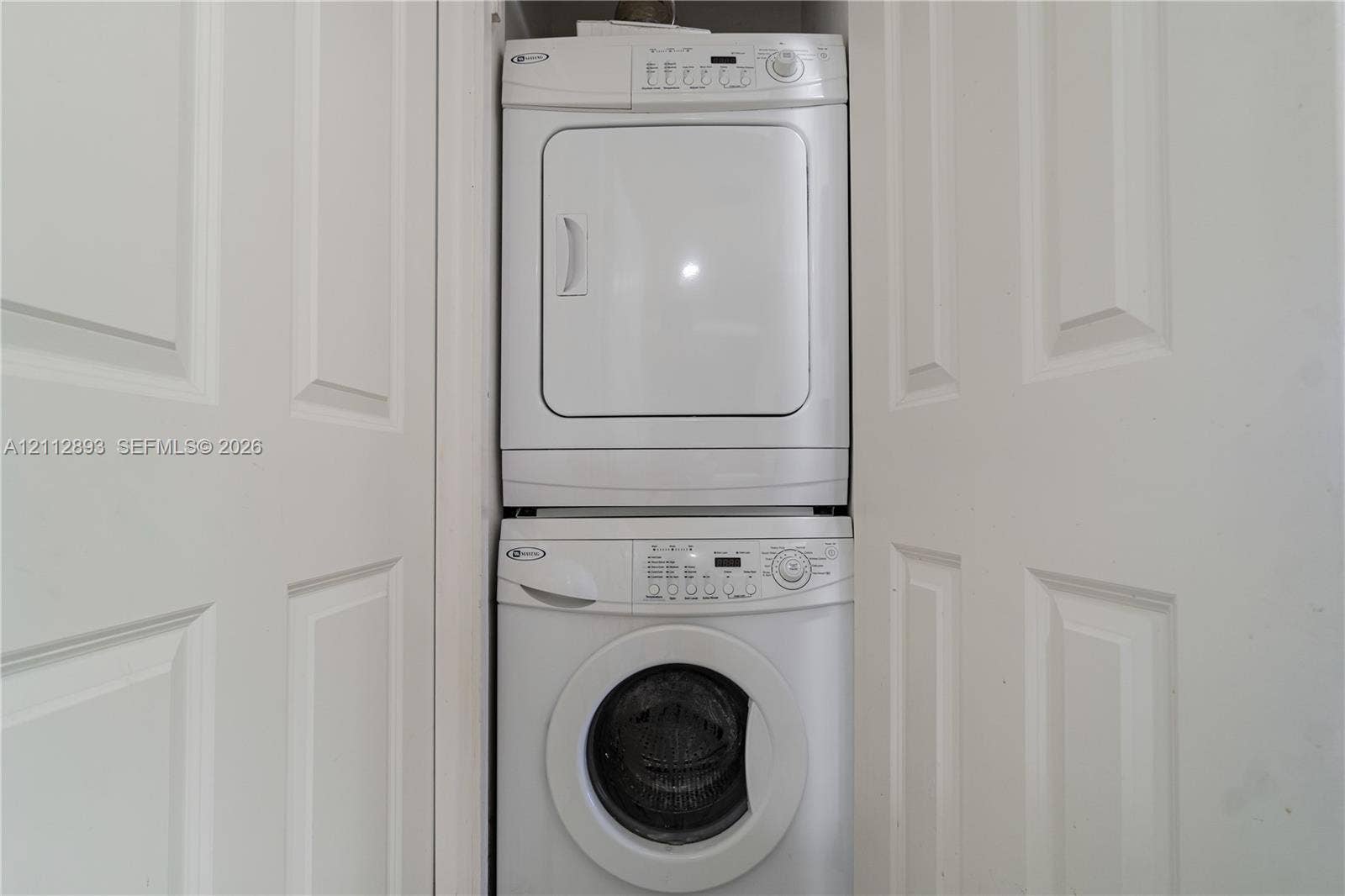 20515 E Country Club Drive, #1048, Aventura, FL 33180 Stackable laundry unit featuring a white front-loading washing machine and a matching dryer, enclosed by white paneled closet doors