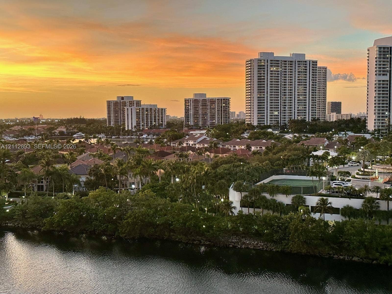 20515 E Country Club Drive, #1048, Aventura, FL 33180 Elevated perspective featuring high-rise architecture, a waterway, mature tropical landscaping, and a tennis court