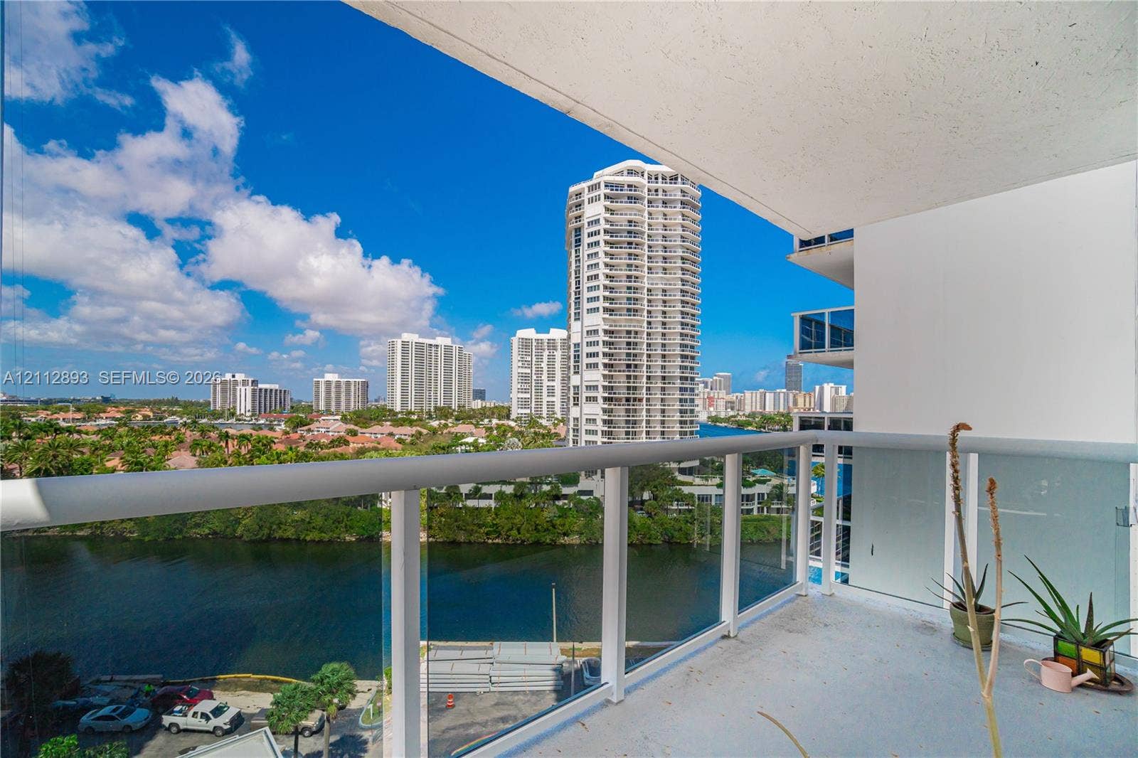20515 E Country Club Drive, #1048, Aventura, FL 33180 Covered balcony featuring glass panel railings and a tubular white metal handrail, offering exposure to the surrounding waterway and high-rise architecture