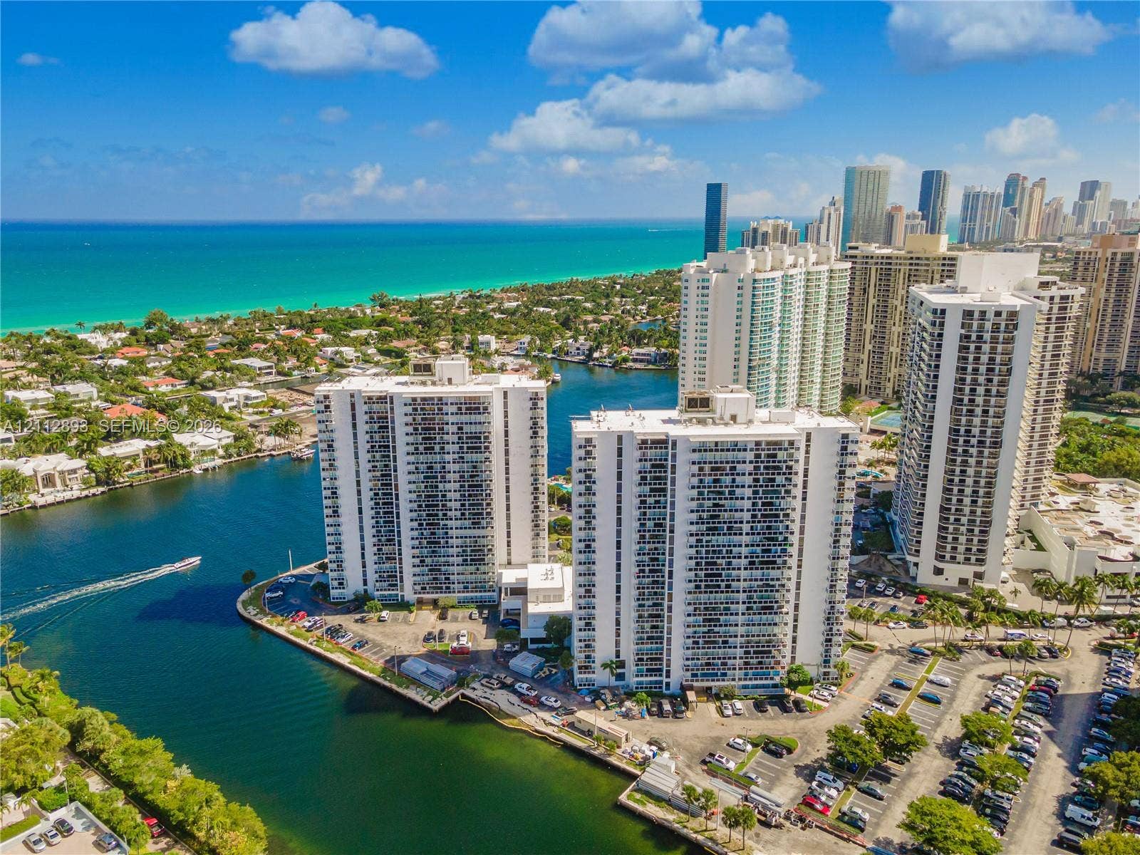 20515 E Country Club Drive, #1048, Aventura, FL 33180 Aerial perspective of high-rise structures situated on a waterfront peninsula with direct coastal access and proximity to urban skyline, featuring on-site surface parking lots and established tropical landscaping