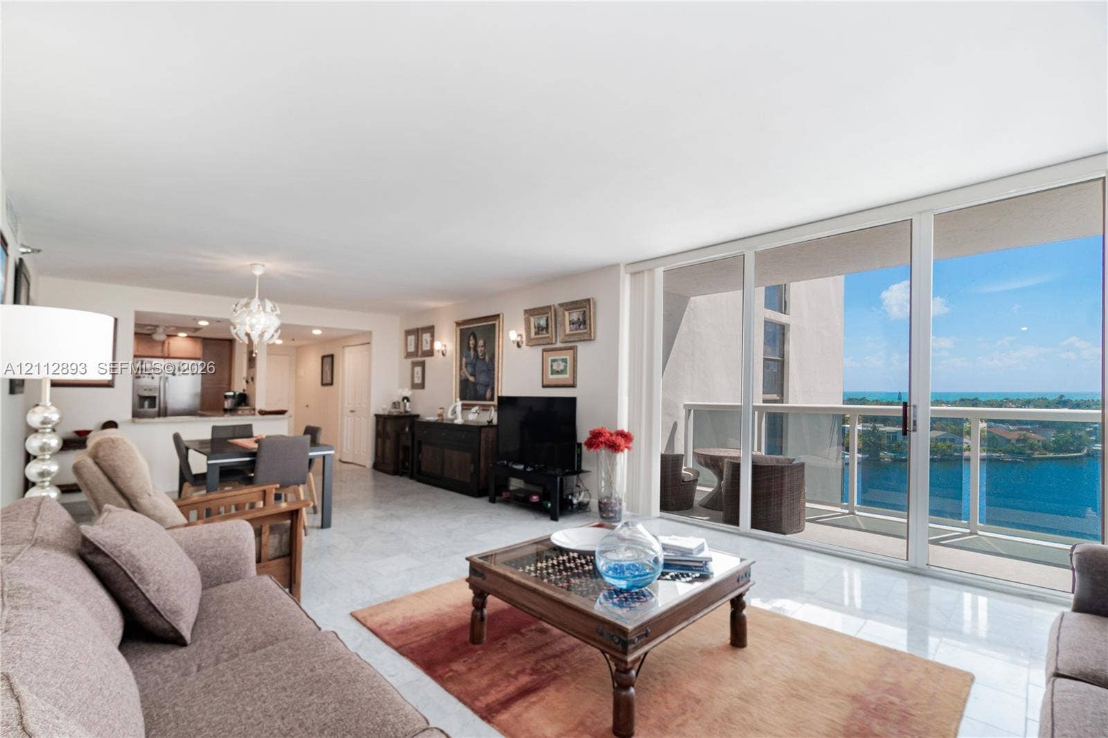 20515 E Country Club Drive, #1048, Aventura, FL 33180 Open-concept living area featuring light-toned tile flooring, floor-to-ceiling sliding glass doors, a balcony with a glass railing, and custom overhead lighting fixtures
