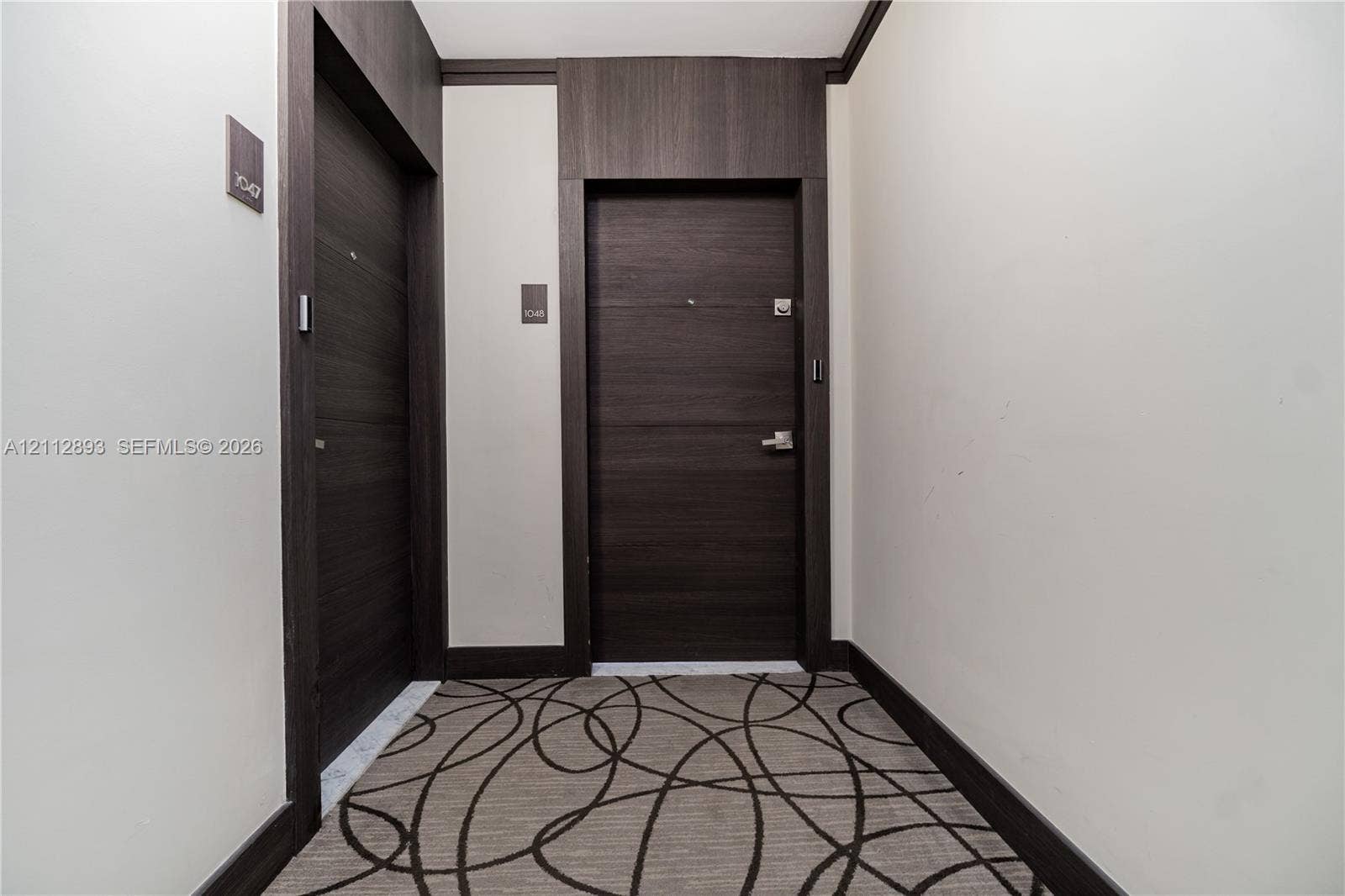 20515 E Country Club Drive, #1048, Aventura, FL 33180 Entryway featuring two dark wood-finish doors with brushed metal hardware, high-contrast dark wood-finish door casing and trim, and patterned wall-to-wall carpeting
