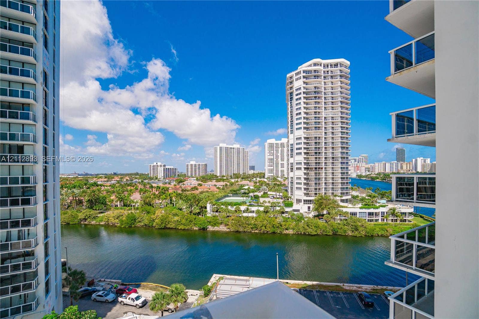 20515 E Country Club Drive, #1048, Aventura, FL 33180 High-rise balcony featuring glass railings, overlooking a waterway, mature landscaping, and an expansive cityscape