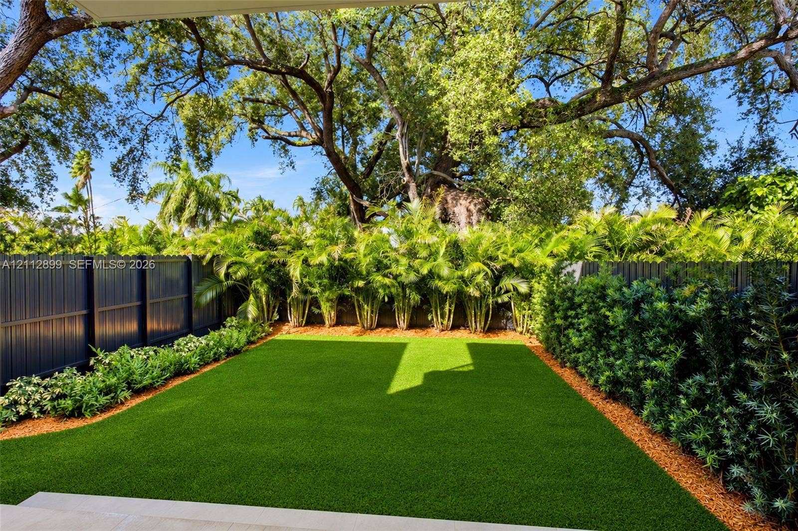2747 SW 23rd Terrace, Miami, FL 33145 Backyard featuring artificial turf, perimeter fencing, mature canopy trees, and dense foliage border