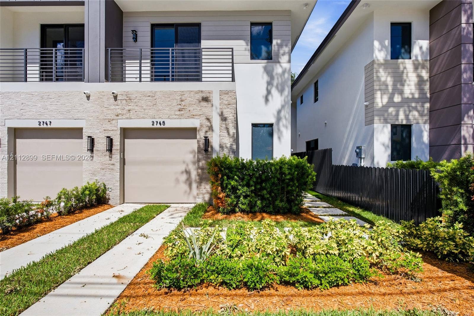 2747 SW 23rd Terrace, Miami, FL 33145 Modern exterior featuring stone veneer siding, a second-story balcony with metal railings, horizontal lap siding, and a concrete driveway with a central grass strip