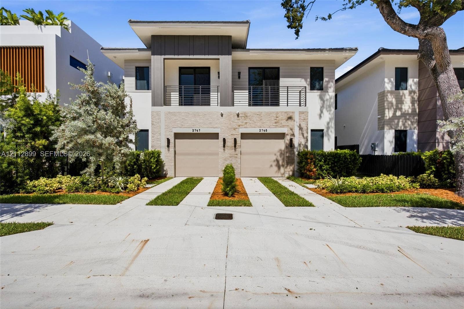 2747 SW 23rd Terrace, Miami, FL 33145 Contemporary two-story exterior featuring a horizontal-slat facade, stone veneer detailing, metal balcony railing, and two integrated garage doors