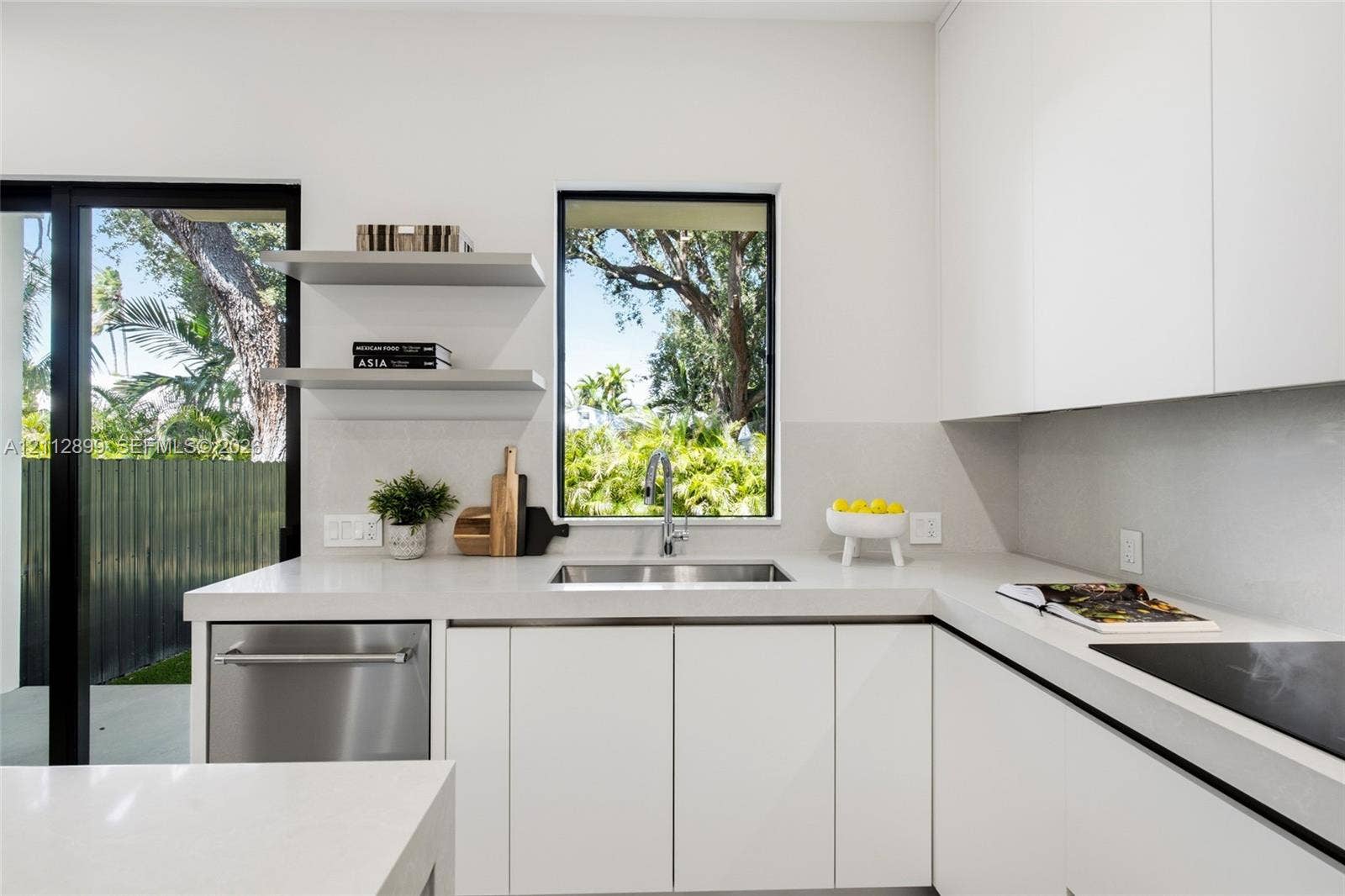 2747 SW 23rd Terrace, Miami, FL 33145 Minimalist kitchen featuring matte white flat-panel cabinetry, light-toned stone-surface countertops, stainless steel undermount sink, built-in dishwasher, and floating wall shelves