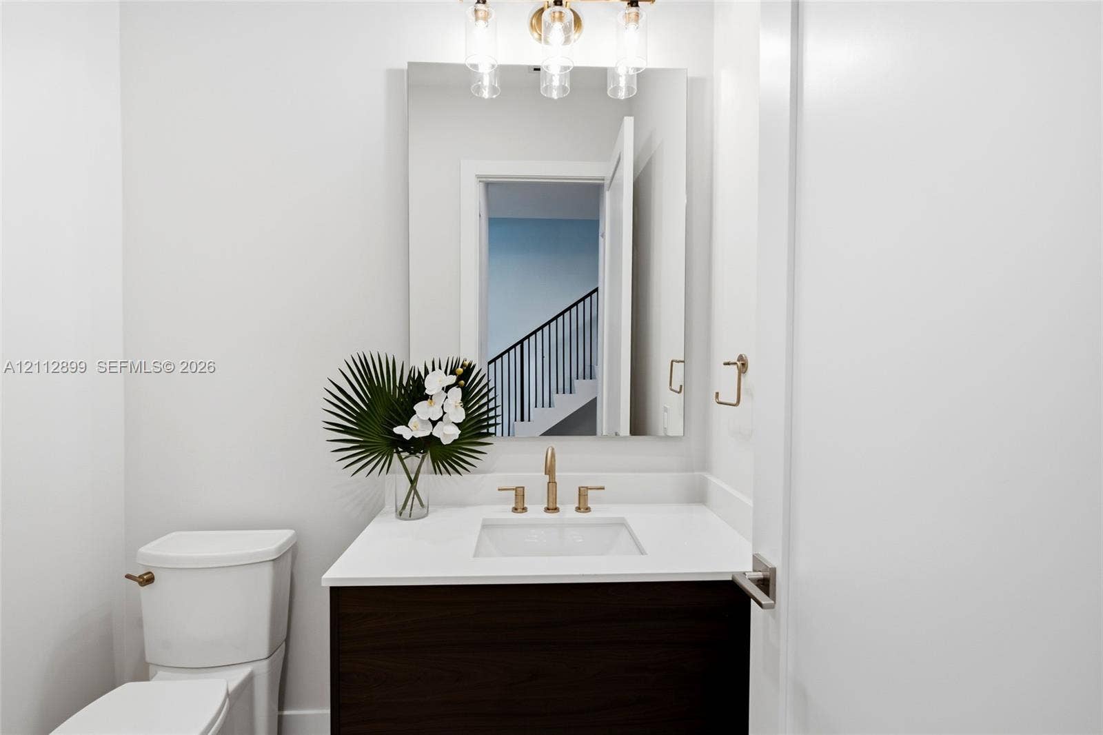 2747 SW 23rd Terrace, Miami, FL 33145 Bathroom featuring a dark wood-finish vanity, white countertop with an integrated basin, wall-mounted rectangular mirror, three-light fixture with cylindrical glass shades, and gold-tone hardware