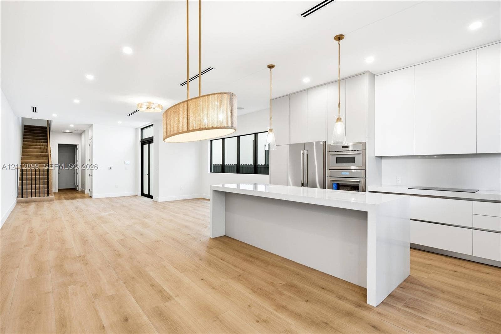 2747 SW 23rd Terrace, Miami, FL 33145 Modern kitchen featuring flat-panel cabinetry, a waterfall-edge quartz island, stainless steel built-in appliances, decorative pendant lighting, and wood-finish flooring