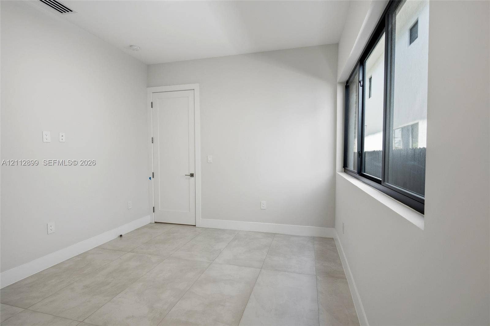2747 SW 23rd Terrace, Miami, FL 33145 Room featuring large-format ceramic tile flooring, neutral wall paint, and a multi-pane window with dark frames