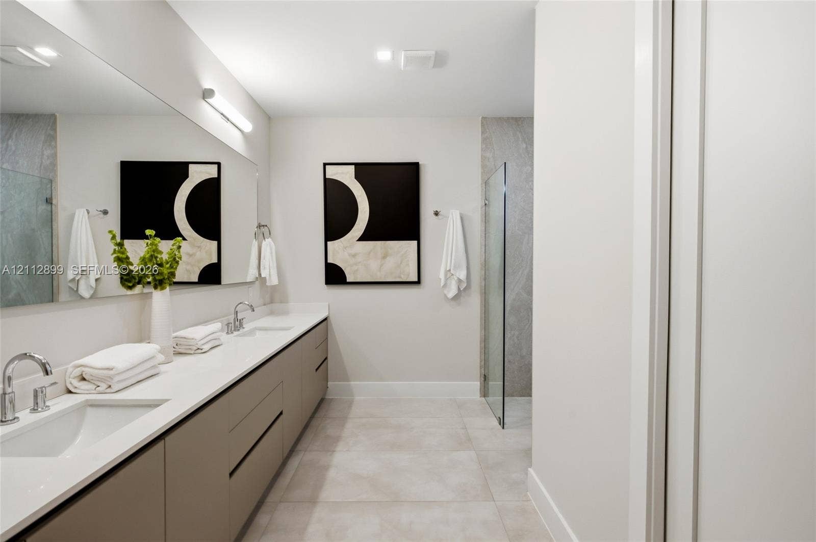 2747 SW 23rd Terrace, Miami, FL 33145 Dual-sink floating vanity with neutral cabinetry, expansive wall-mounted mirror, light-toned stone-finish flooring, and glass-enclosed shower with full-height stone-finish wall cladding