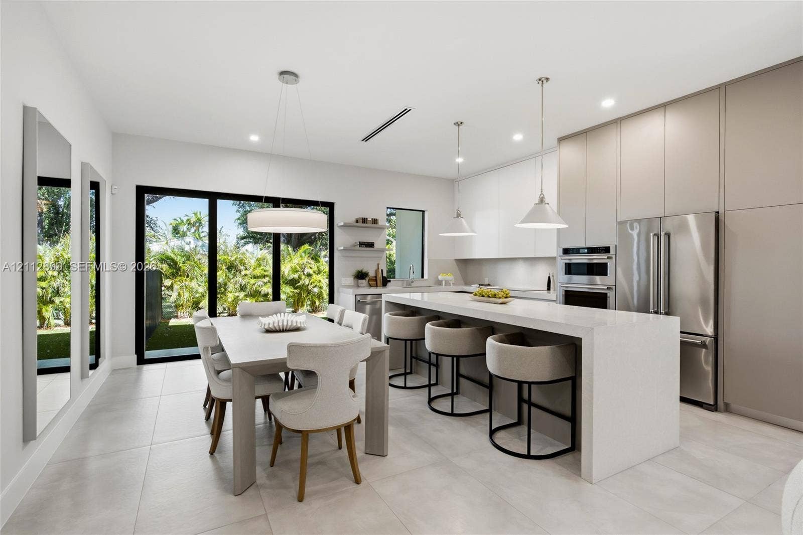 2747 SW 23rd Terrace, Miami, FL 33145 Kitchen featuring a waterfall-edge island with solid-surface countertops, floor-to-ceiling flat-panel cabinetry, stainless steel built-in appliances, pendant lighting, and large-format porcelain tile flooring
