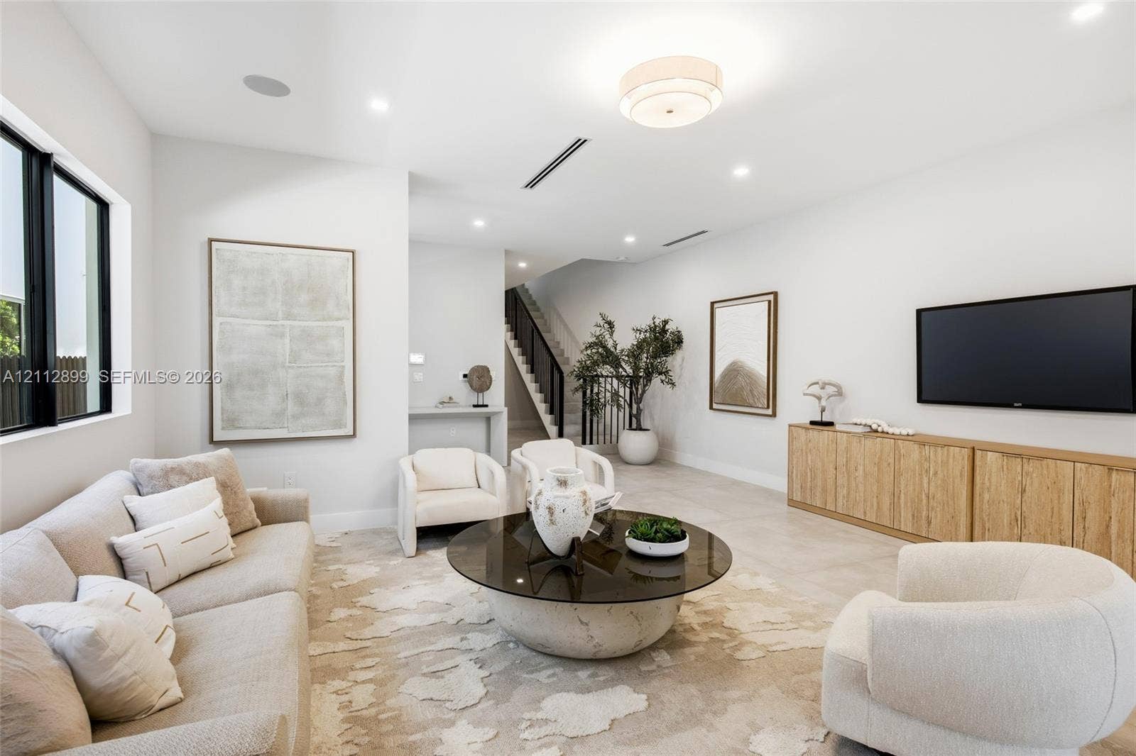 2747 SW 23rd Terrace, Miami, FL 33145 Open-concept living space featuring neutral oversized tile flooring, recessed ceiling lighting, a contemporary flush-mount fixture, black-framed windows, and built-in wood-finish cabinetry