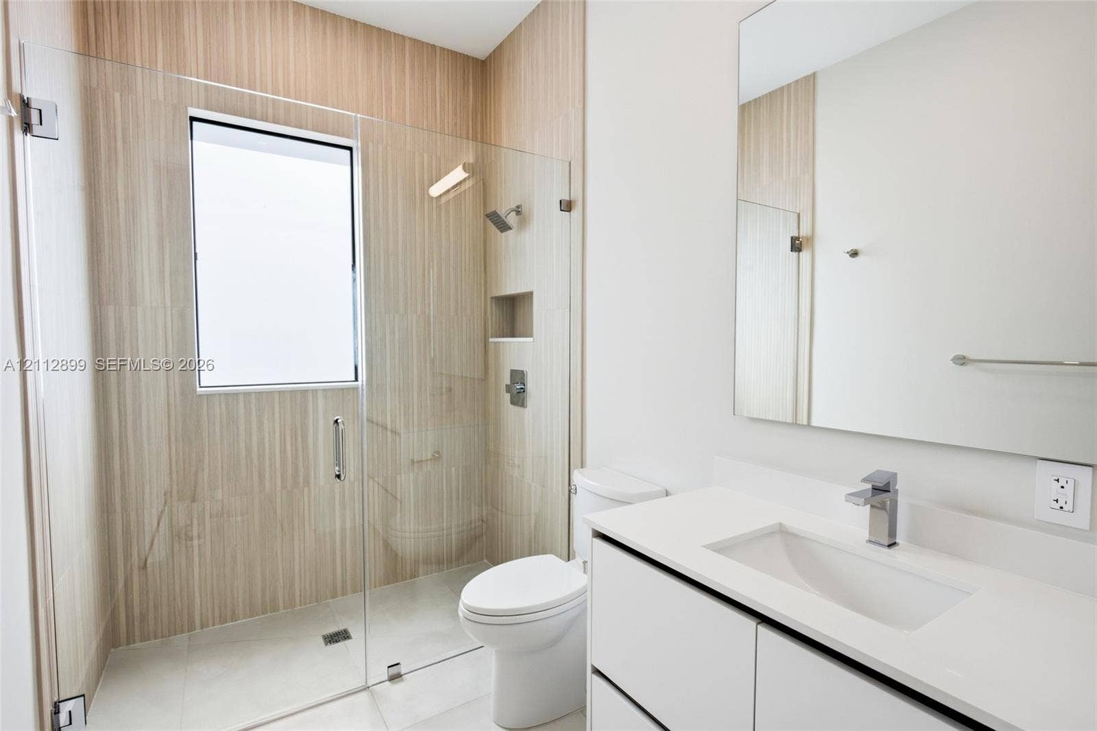 2747 SW 23rd Terrace, Miami, FL 33145 Modern bathroom featuring a glass-enclosed shower with vertical-tile surround, built-in recessed wall niche, wall-to-wall mirror, and white vanity with stone-finish countertop