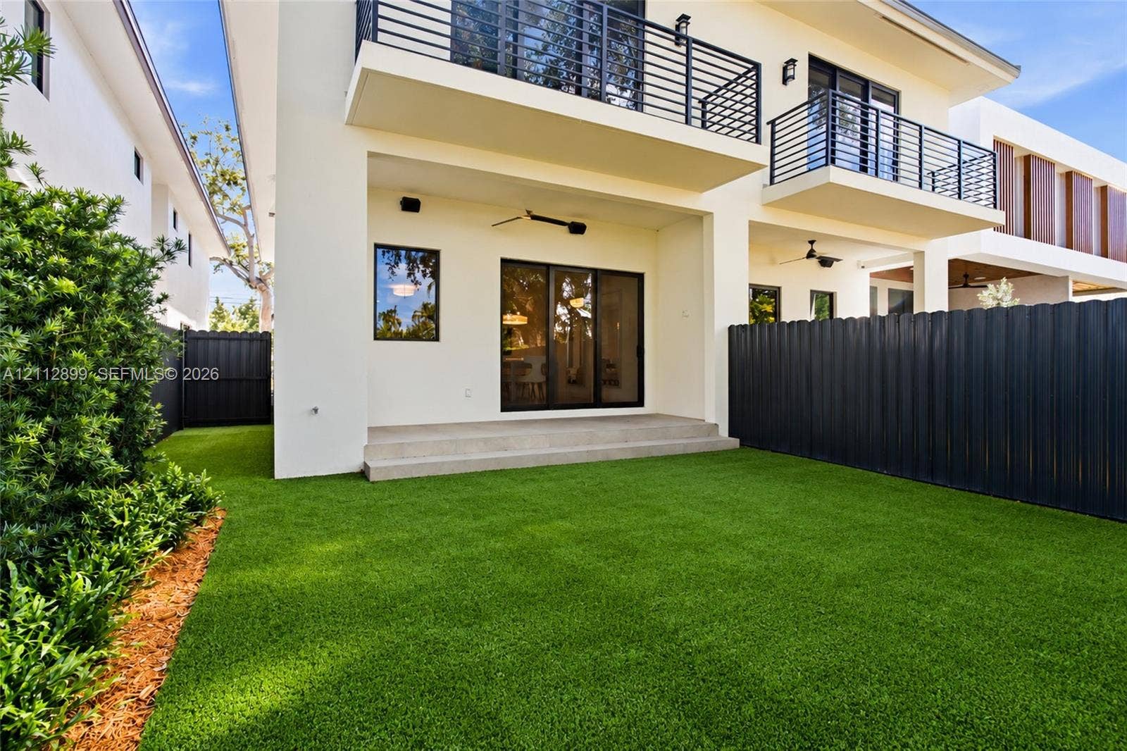 2747 SW 23rd Terrace, Miami, FL 33145 Rear exterior featuring a concrete patio, synthetic turf lawn, privacy fencing, and second-level balcony with metal railings