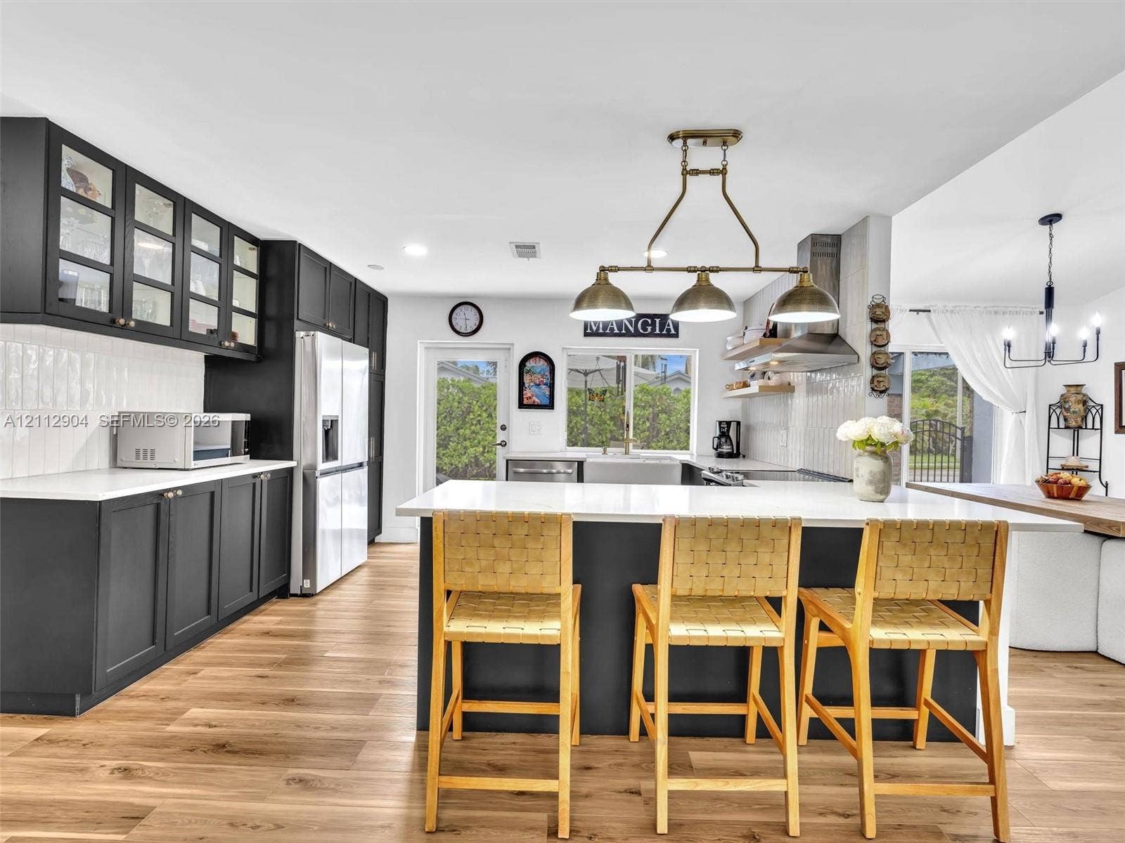 76 Forest Circle, Cooper City, FL 33026 Kitchen featuring flat-panel cabinetry with glass-front uppers, a central island with a solid-surface countertop, wood-finish flooring, and multi-bulb pendant lighting