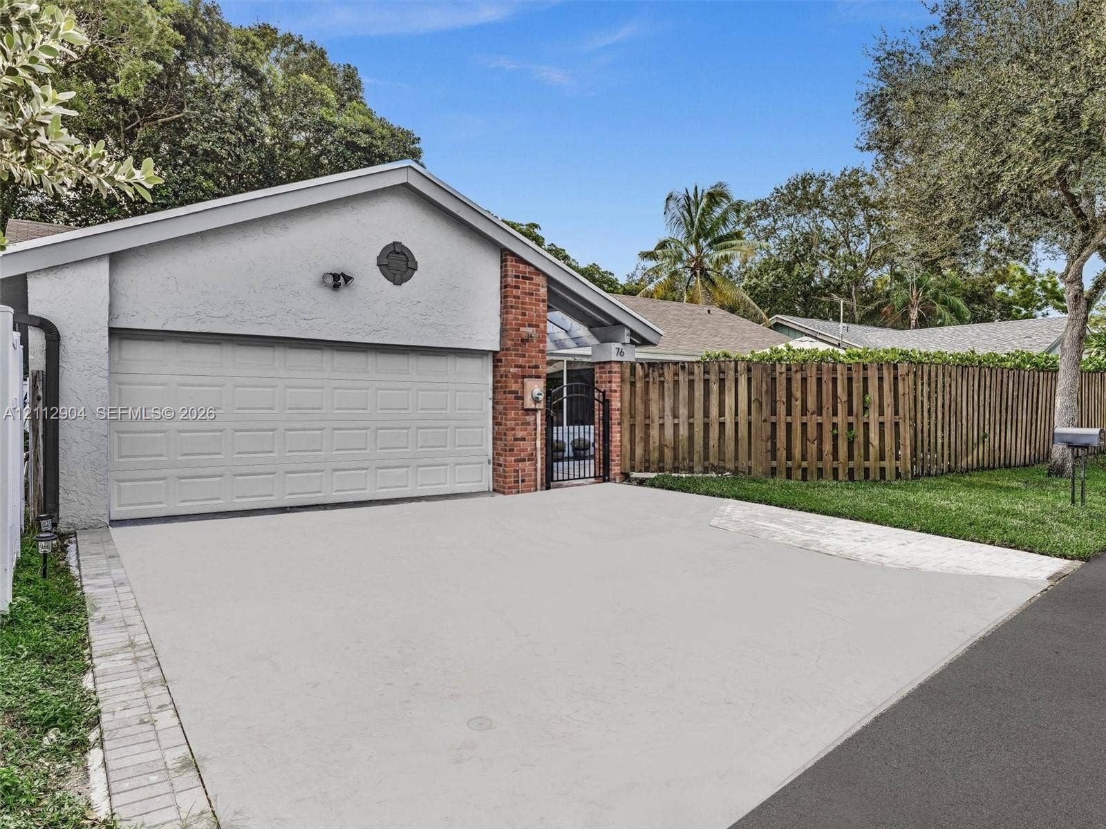 76 Forest Circle, Cooper City, FL 33026 Single-story residence featuring a stucco facade, red brick accent siding, attached two-car garage, and wood-panel privacy fencing