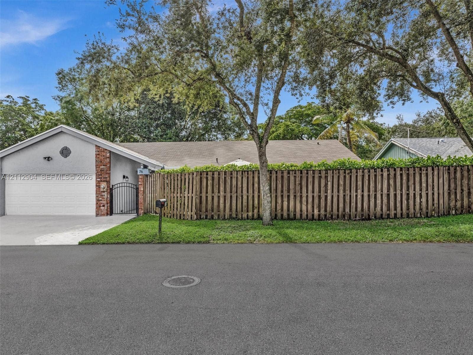 76 Forest Circle, Cooper City, FL 33026 Single-story exterior featuring a stucco facade, red brick accents, an attached garage, and a wood privacy fence