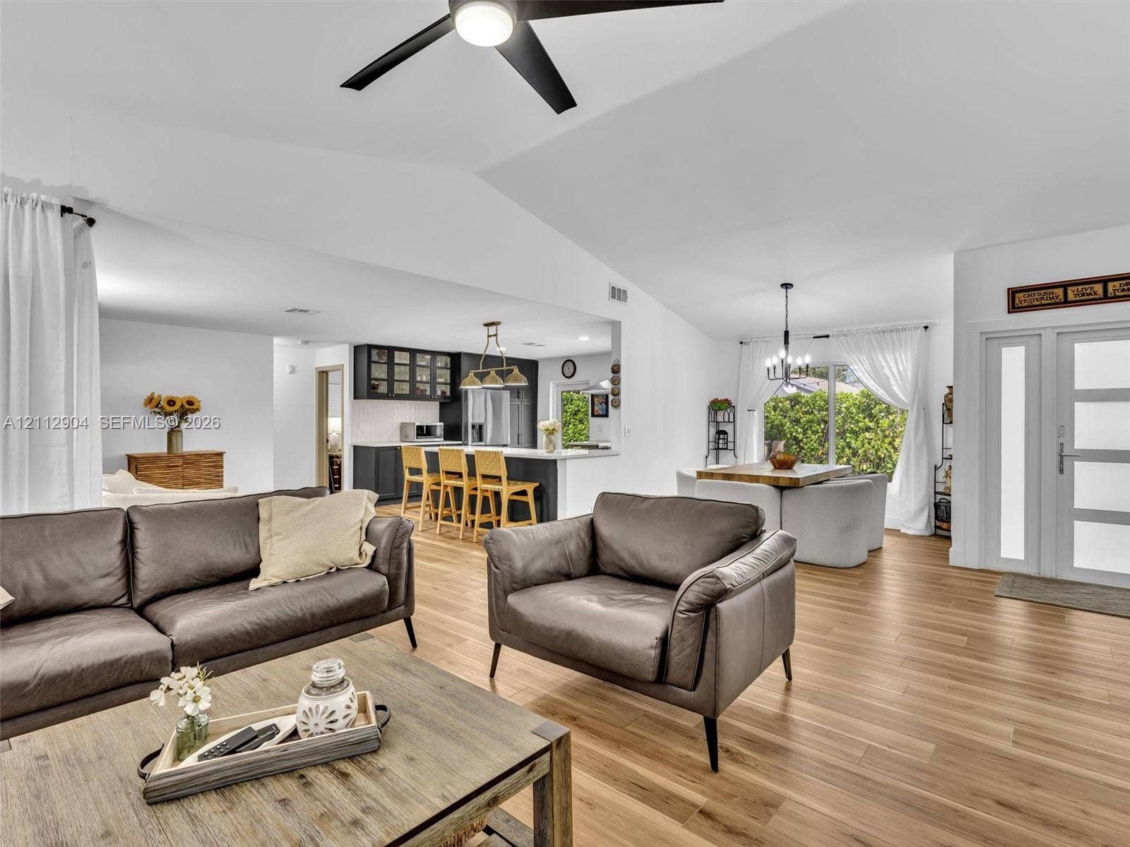 76 Forest Circle, Cooper City, FL 33026 Open-concept interior featuring vaulted ceilings, wood-finish flooring, a kitchen island with built-in cabinetry, a multi-pane glass entry door, and a modern ceiling fan