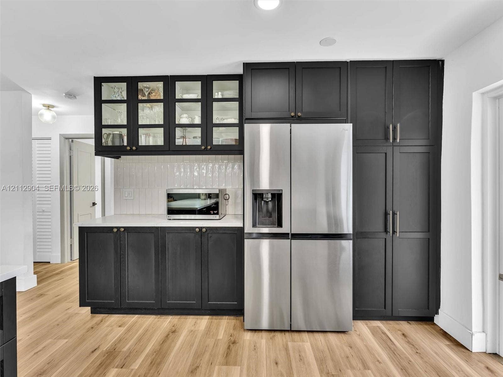 76 Forest Circle, Cooper City, FL 33026 Custom cabinetry featuring glass-front upper storage, matte-finish lower cupboards, floor-to-ceiling pantry units, integrated stainless steel refrigeration, and wood-finish flooring