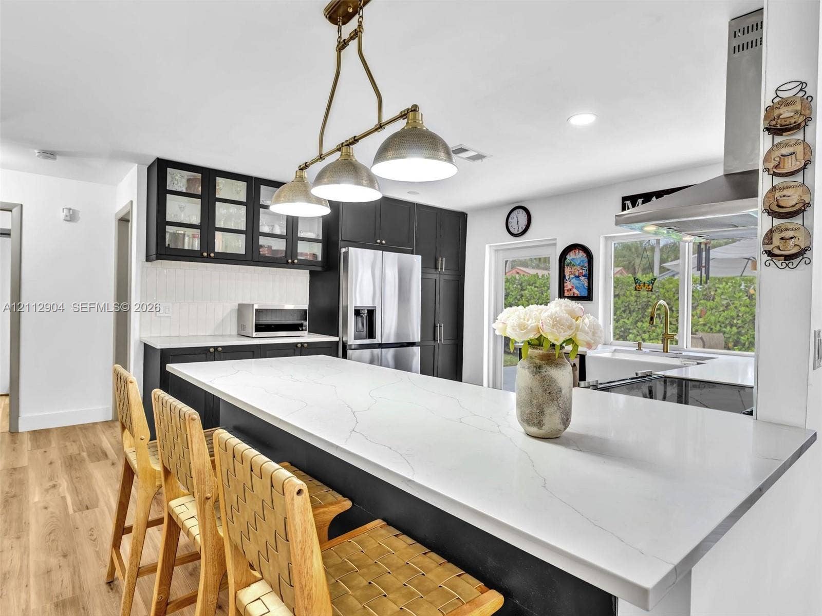 76 Forest Circle, Cooper City, FL 33026 Kitchen featuring dark cabinetry with glass-panel upper doors, a large kitchen island with a stone-finish countertop, stainless steel appliances, a multi-pendant light fixture, and wood-finish flooring