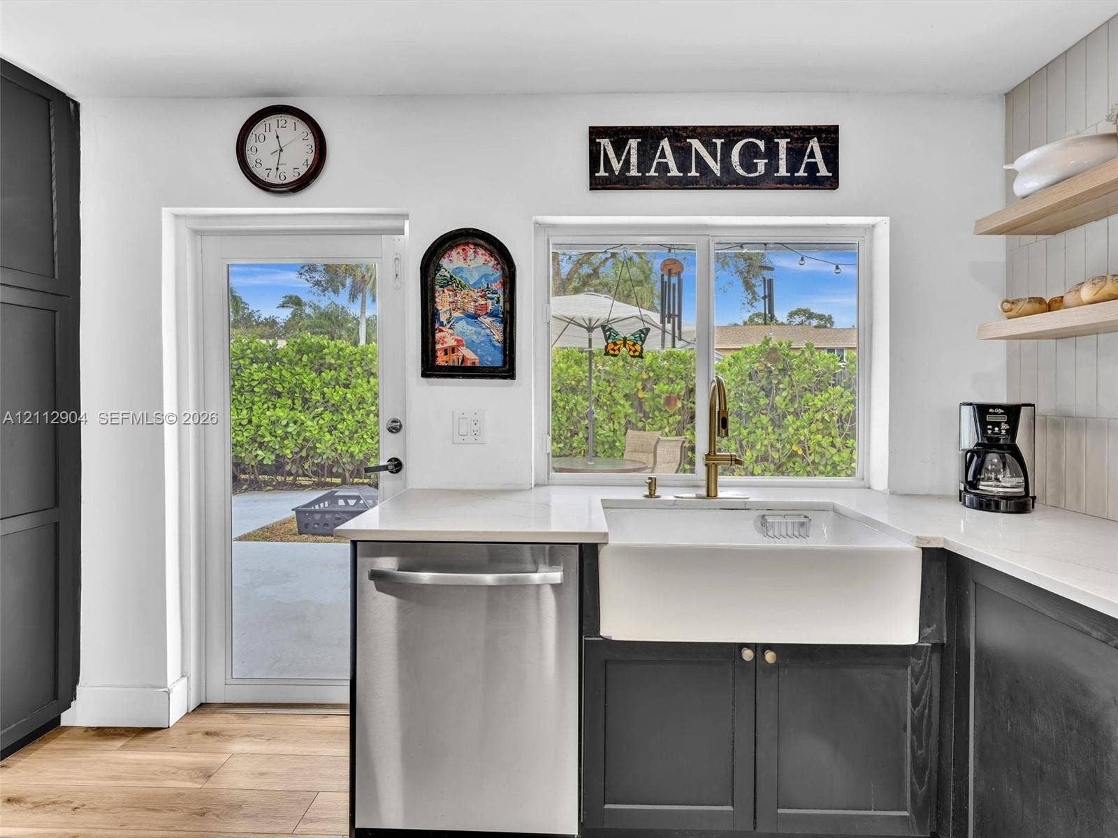 76 Forest Circle, Cooper City, FL 33026 Kitchen featuring charcoal-toned lower cabinetry, white apron-front sink with gold-tone fixture, light-toned quartz countertops, wood-finish flooring, and floating wood shelving
