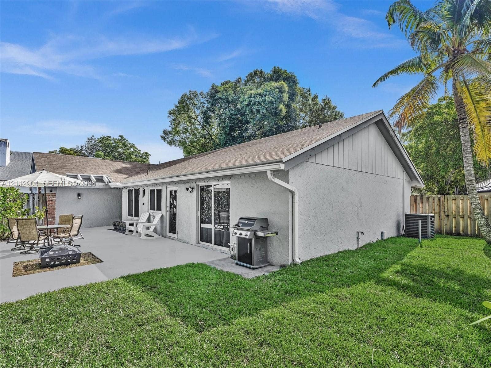 76 Forest Circle, Cooper City, FL 33026 Stucco exterior with a rear concrete patio, sliding glass door, and fenced backyard featuring mature palm trees