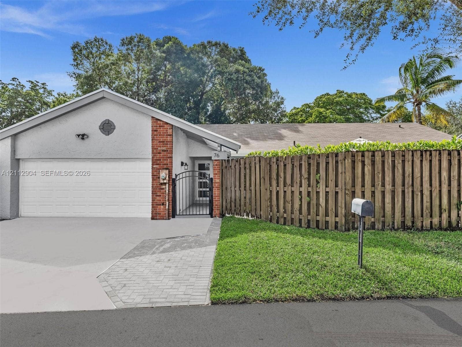 76 Forest Circle, Cooper City, FL 33026 Exterior facade featuring a stucco finish, brick accents, attached garage, paved walkway, and wood-slat privacy fencing