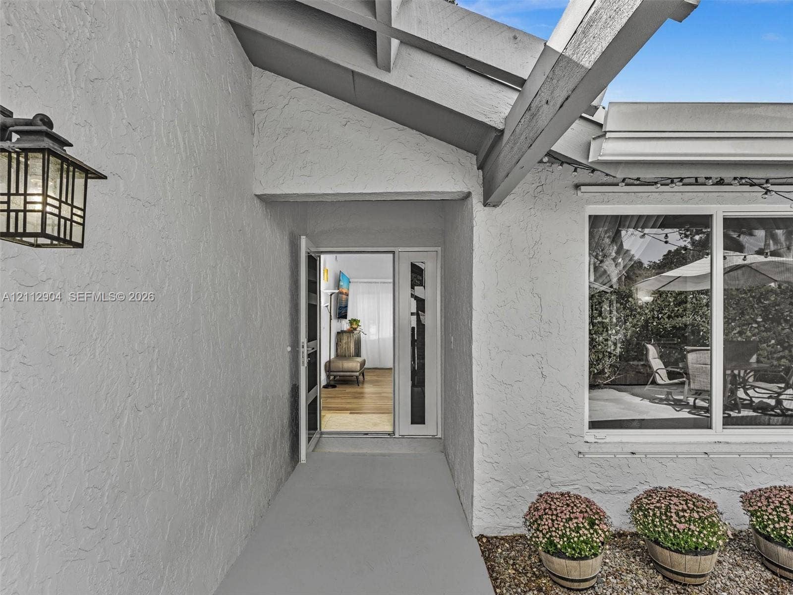76 Forest Circle, Cooper City, FL 33026 Covered entryway featuring textured stucco exterior, exposed rafters, decorative lantern-style wall lighting, and a glass-paneled front door